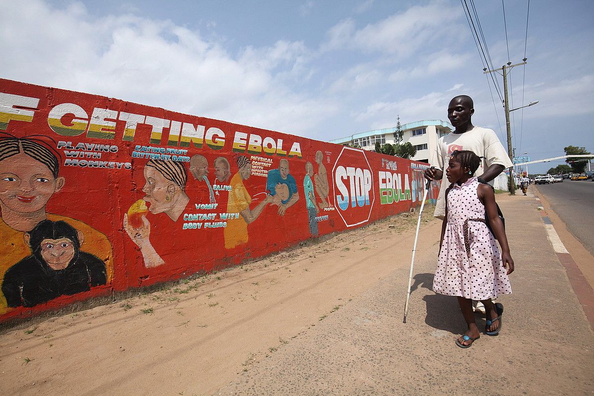 Gizonezko bat eta neska gazte bat Ebolari buruzko pintaketa bati begira, 2015eko abuztuan, Liberiako Monrovia hirian. AHMED JALLANZO / EFE.