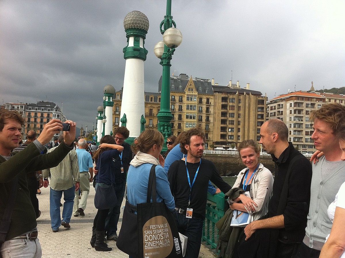 Kursaala eta Maria Cristina lotzen dituen zubian, lagun talde bat, kreditazioa eta Zinemaldiko poltsak gainean dituztela. XABIER MARTIN. Kursaala eta Maria Cristina lotzen dituen zubian, lagun talde bat, kreditazioa eta Zinemaldiko poltsak gainean dituztela. XABIER MARTIN.