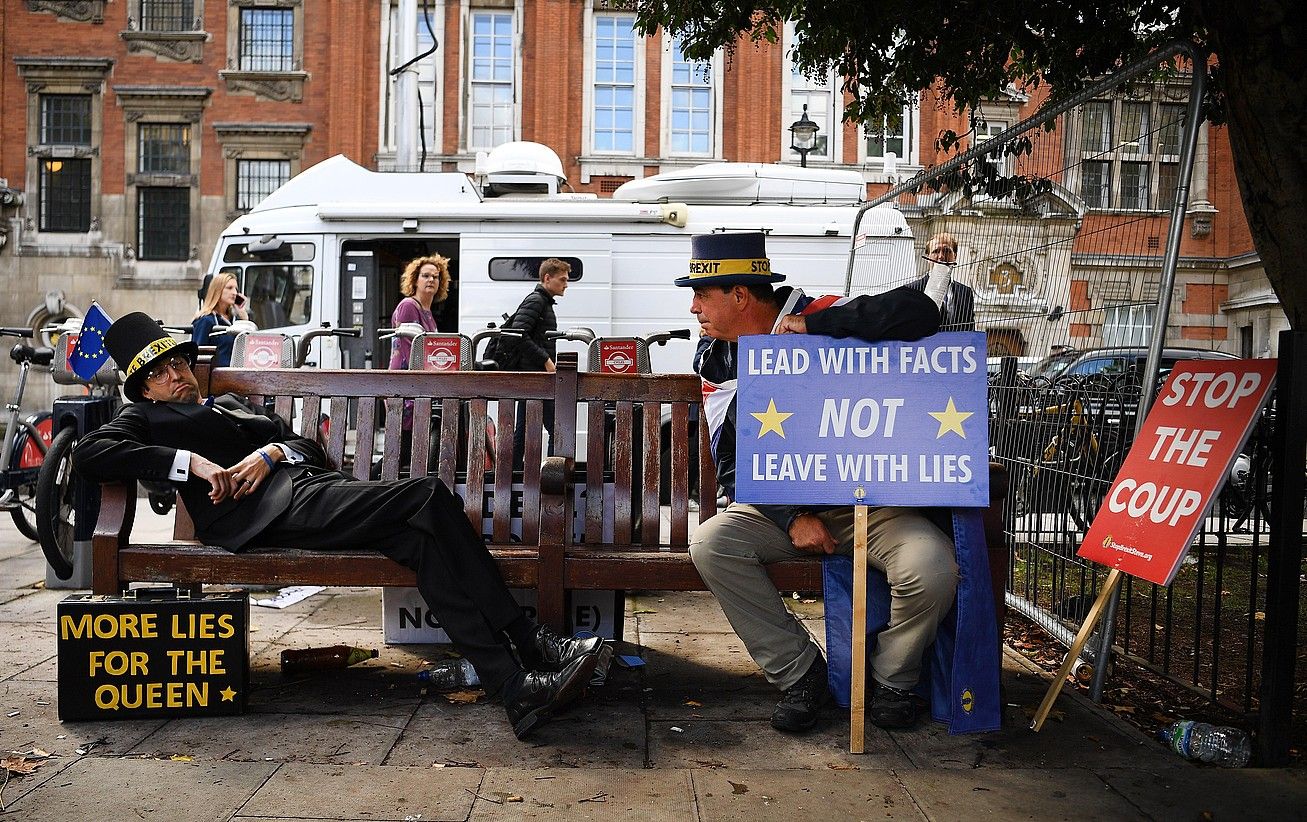 Brexit-aren aurkako manifestari bat —ezkerrekoa— Jacob Rees Mogg diputatu torya bezperan parlamentuko besaulkian etzan zeneko unea imitatzen, atzo, Londresen. ANDY RAIN / EFE.