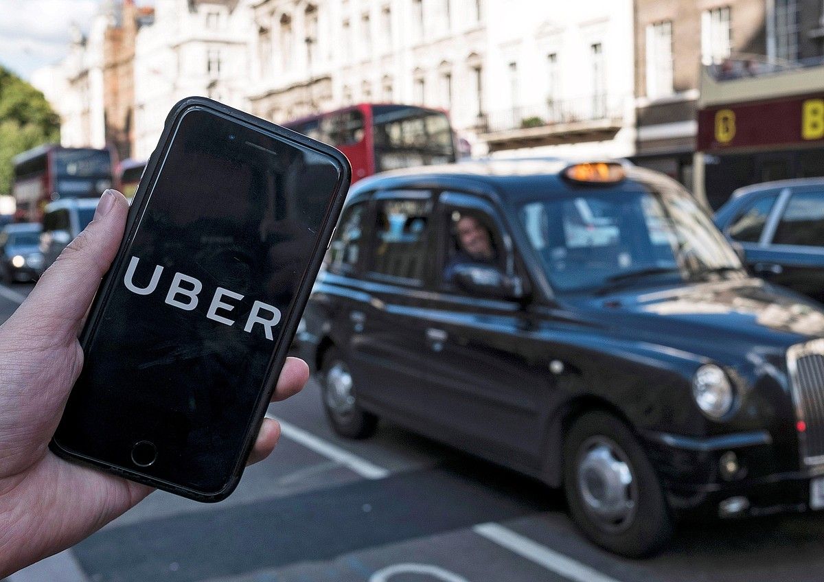 Taxi tradizional bateko gidaria Londresen, Uber aplikazioa duen sakelako baten jabeari begira. WILL OLIVER / FOKU.
