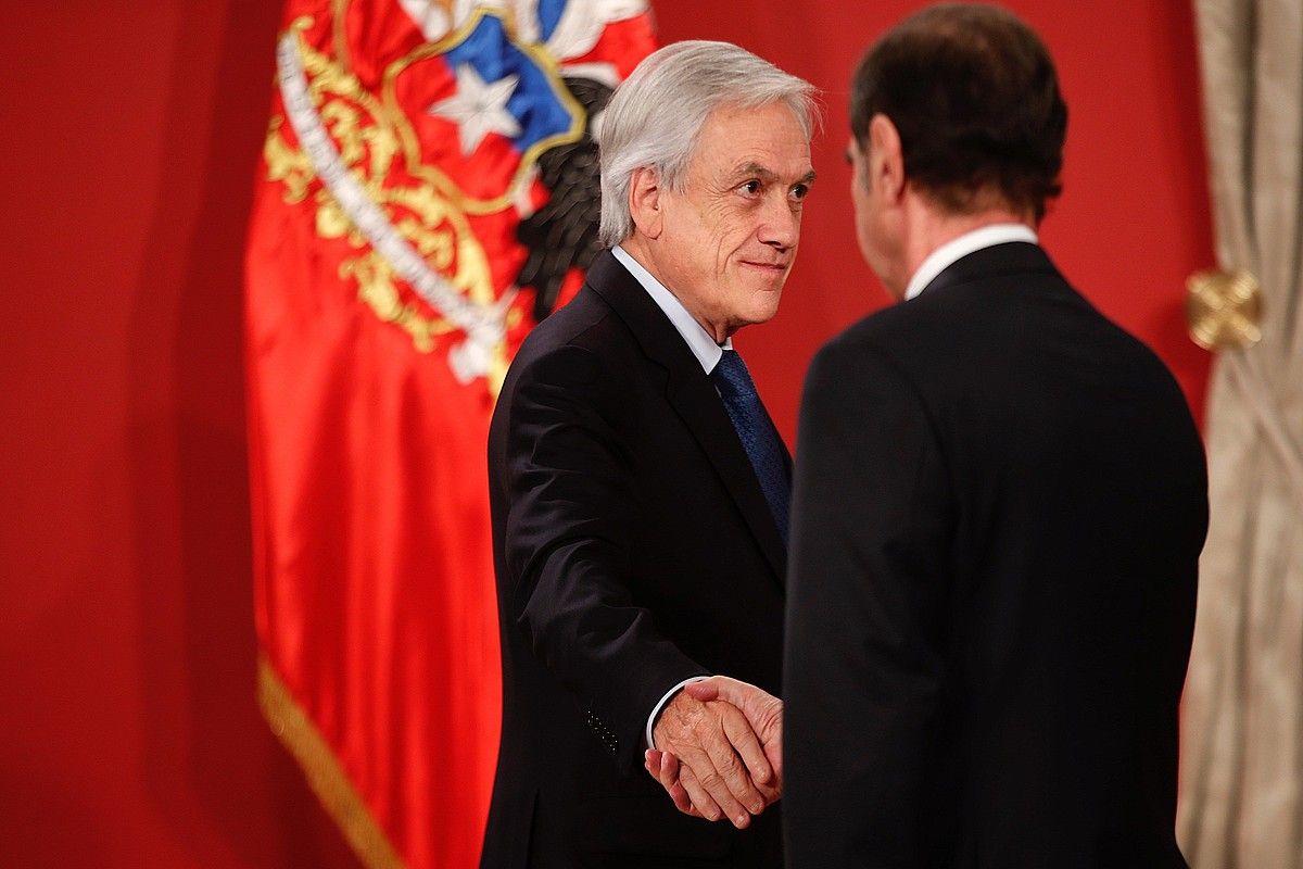 Sebastian Piñera Txileko presidentea, atzo, Hernan Larrain Justizia ministroari —bizkarrez— eskua ematen. ALBERTO VALDES / EFE.