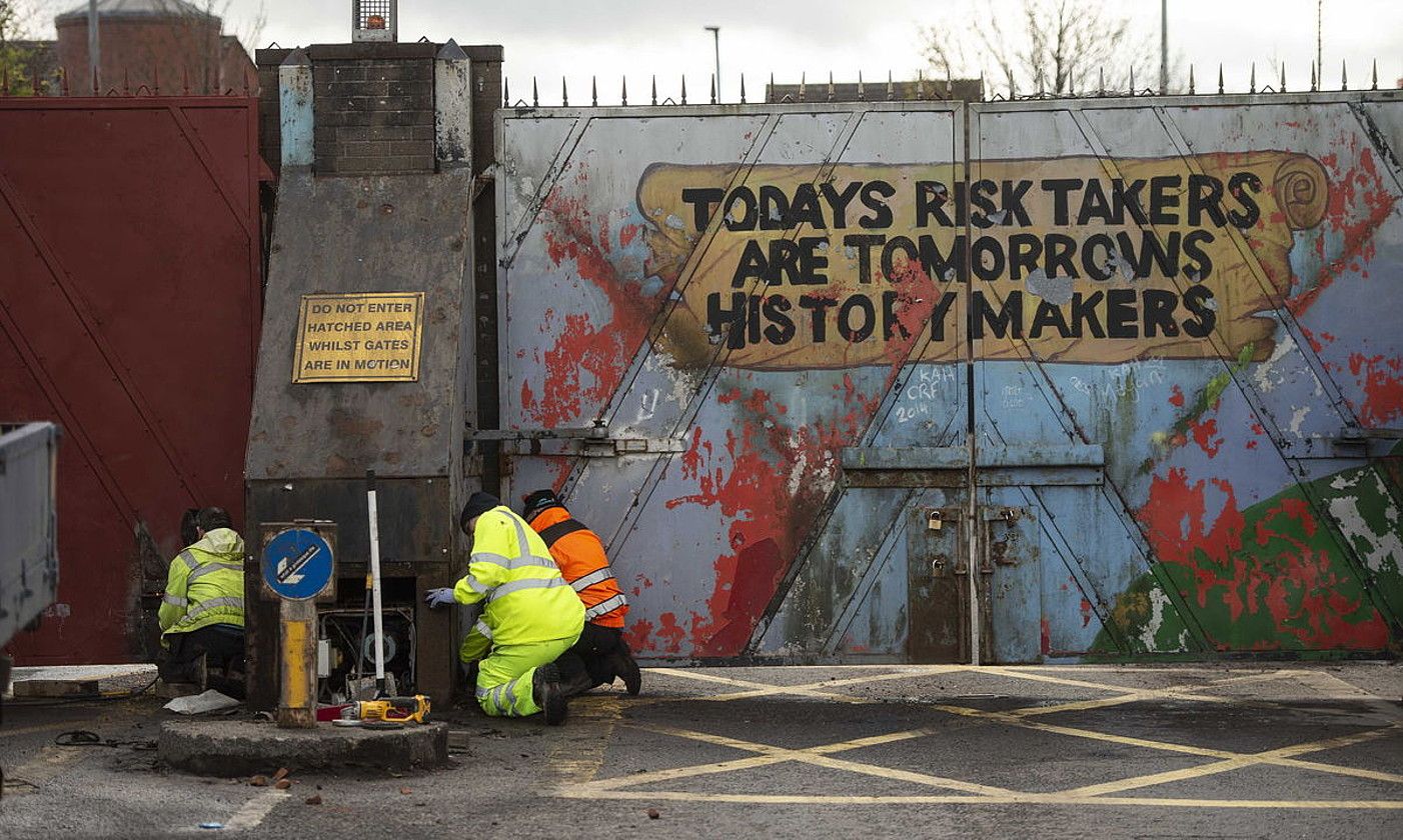 Hiru langile Belfast mendebaldeko auzo nazionalistaren eta unionistaren arteko atea konpontzeko lanetan, atzo. MARK MALOW / EFE.