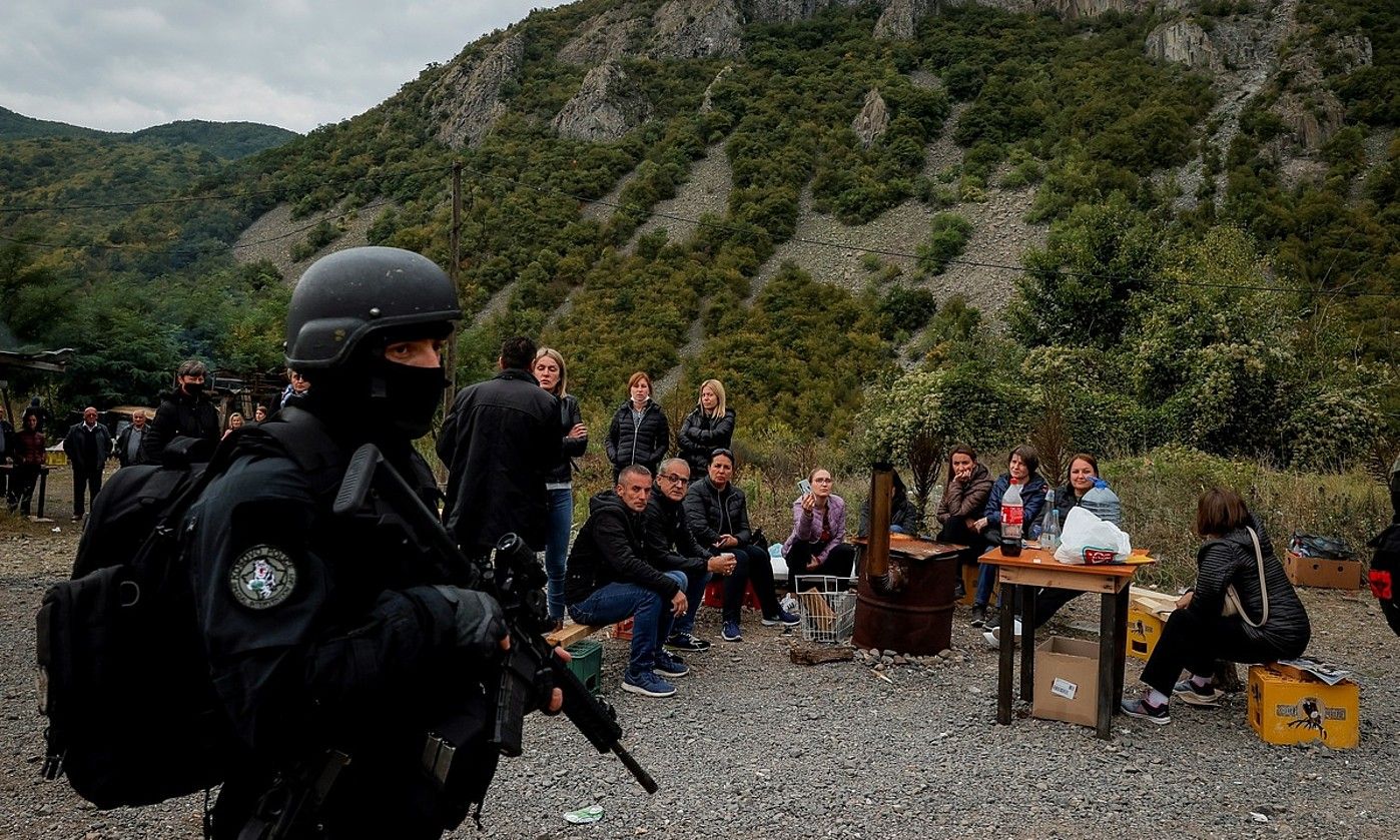 Kosovoko Poliziaren agente bat Jarinje pasabidean, joan den astean, alboan Kosovoko serbiarren talde bat duela. VALDRIN XHEMAJ / EFE.