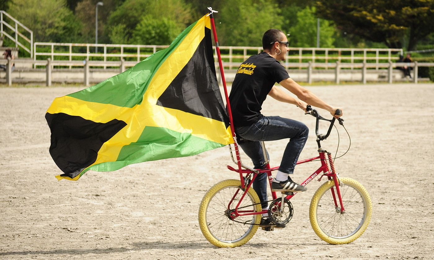 Gizon bat Jamaikako bandera bizikletan jarrita, Iruñerria Jamaica Clashek antolatutako festa batean, 2019an. IRUÑERRIA JAMAICA CLASH.