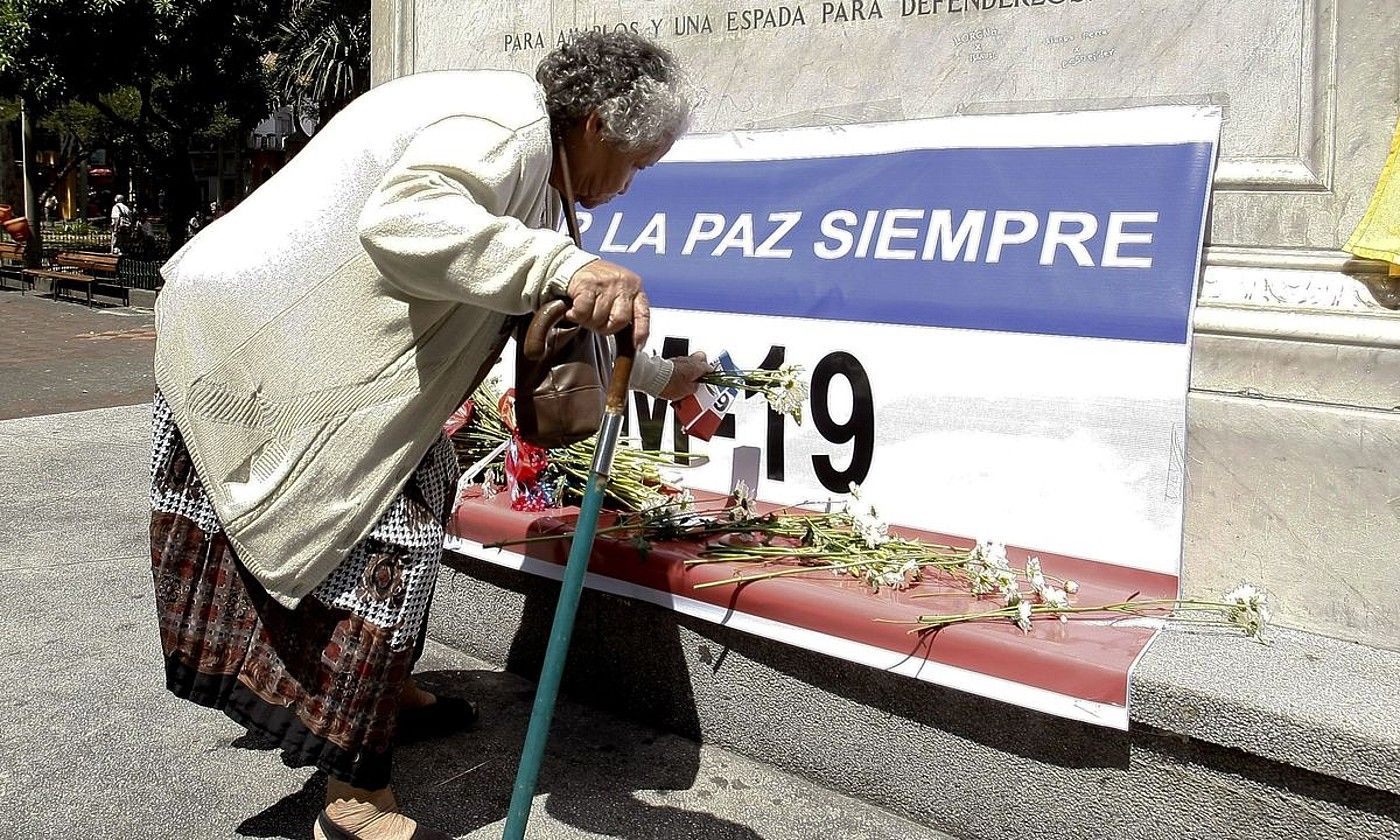 Emakume bat loreak uzten M-19 gerrillari taldearen bandera baten gainean, Medellinen (Kolonbia), 2015ean. LUIS EDUARDO NORIEGA / EFE. Emakume bat loreak uzten M-19 gerrillari taldearen bandera baten gainean, Medellinen (Kolonbia), 2015ean. LUIS EDUARDO NORIEGA / EFE.
