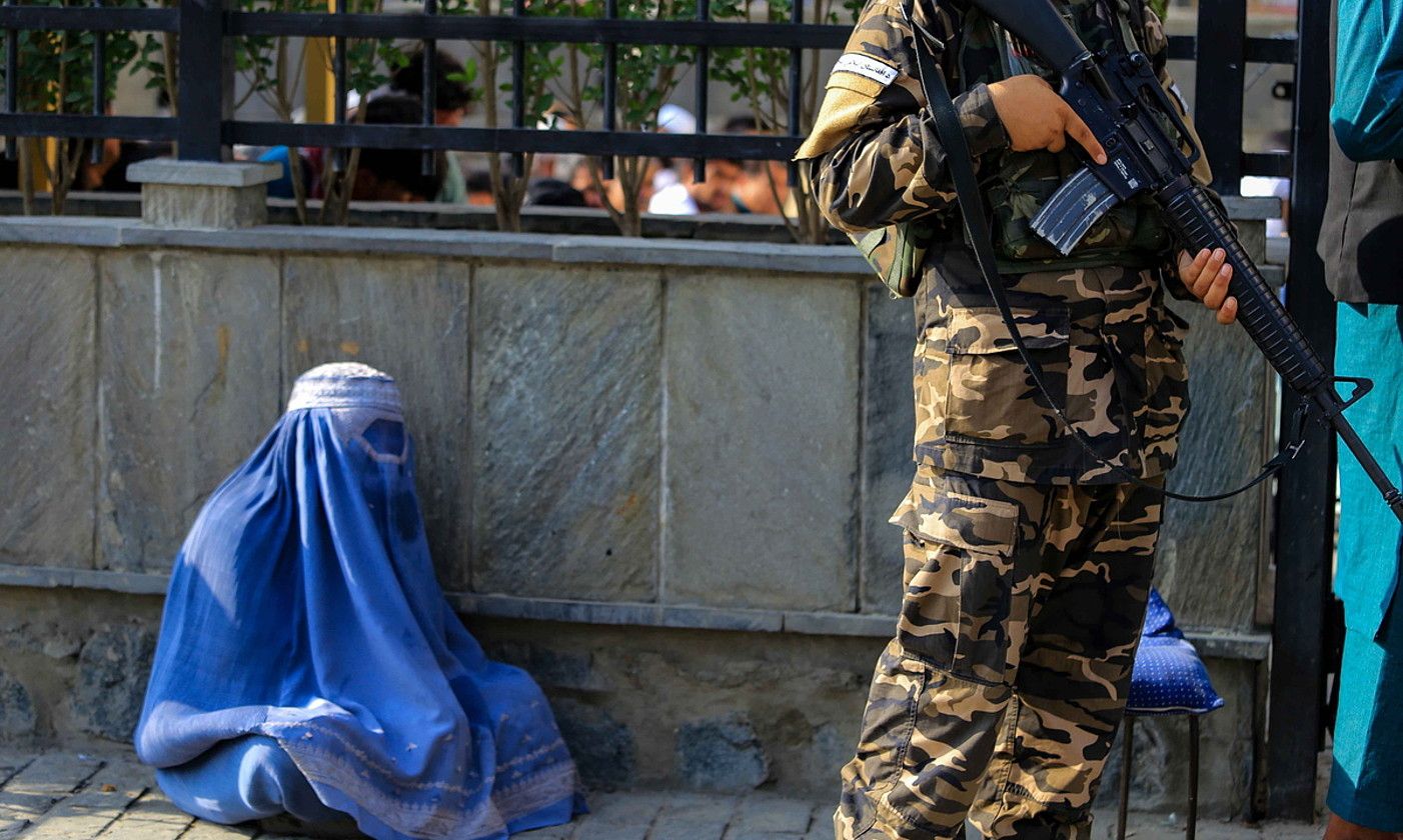 Emakume afganiar bat eskean, soldadu taliban bat aurrean duela, Kabulen. STR / EFE. Emakume afganiar bat eskean, soldadu taliban bat aurrean duela, Kabulen. STR / EFE.