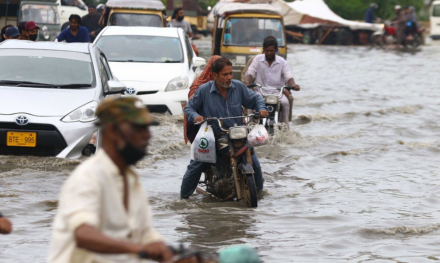 Pakistango herritarrak, montzoi garaiko euriteen ondorioz urak hartutako kaleetan, Karachin. XAHZAIB AKBER / EFE. Pakistango herritarrak, montzoi garaiko euriteen ondorioz urak hartutako kaleetan, Karachin. XAHZAIB AKBER / EFE.
