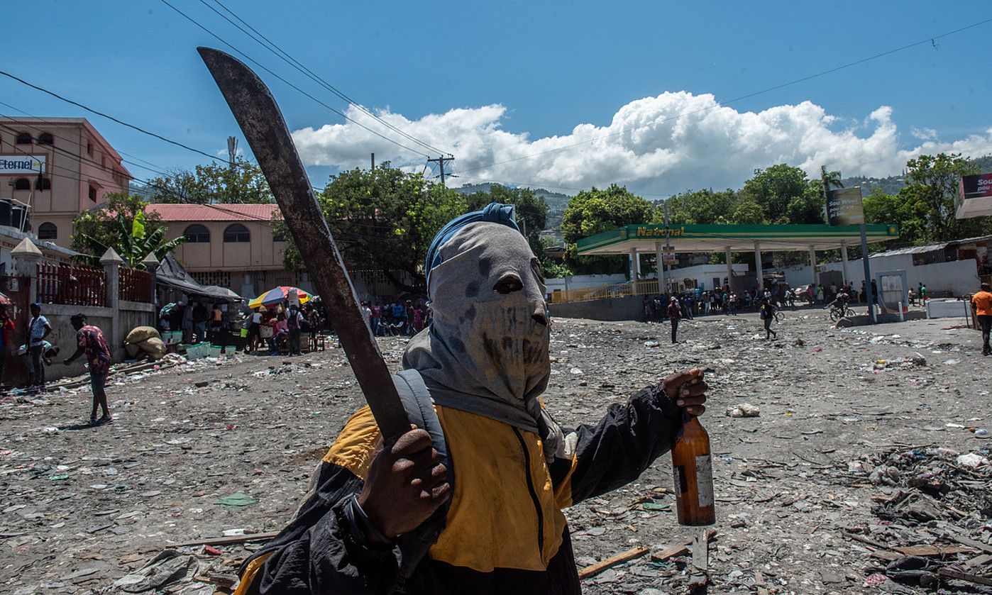 Manifestari bat, aihotz bat eskuetan eta aurpegia estalia duela, herenegun, Port-au-Prince hiriburuan. JOHNSON SABIN / EFE. Manifestari bat, aihotz bat eskuetan eta aurpegia estalia duela, herenegun, Port-au-Prince hiriburuan. JOHNSON SABIN / EFE.