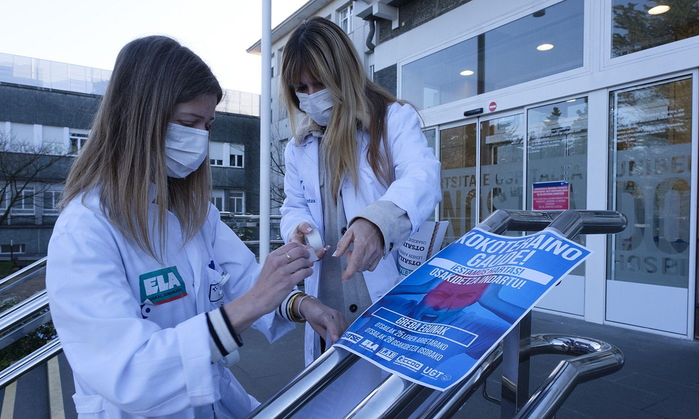 Osakidetzako bi langile greba egun baten berri ematen duen afixa bat jartzen, Donostia ospitaleko sarrera nagusiko eskaileretan. JON URBE / FOKU.