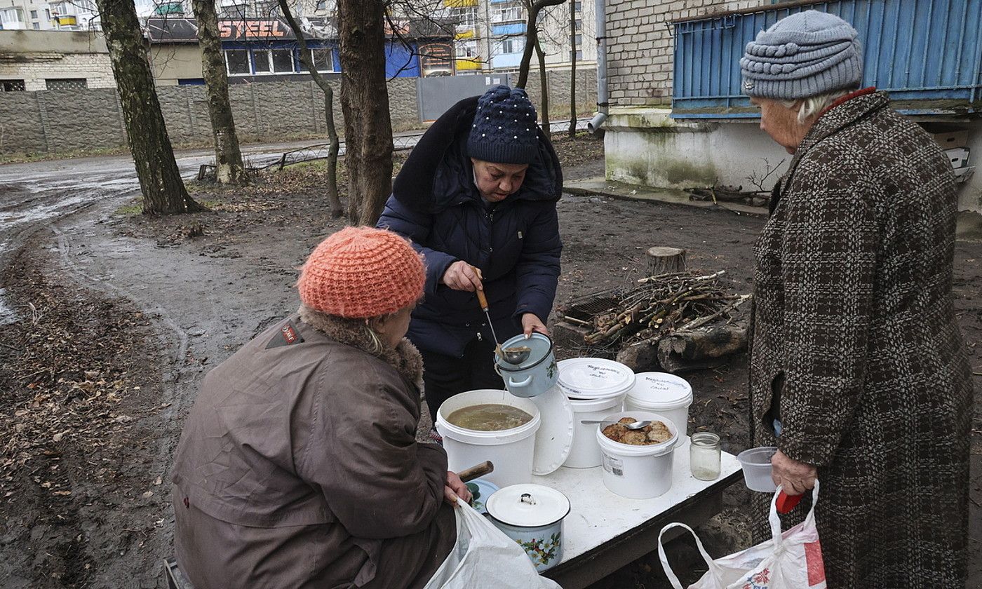 Boluntario bat bi emakumezkori jaki beroak banatzen, atzo, Iziumen (Ukraina). SERGIY KOZLO / EFE.