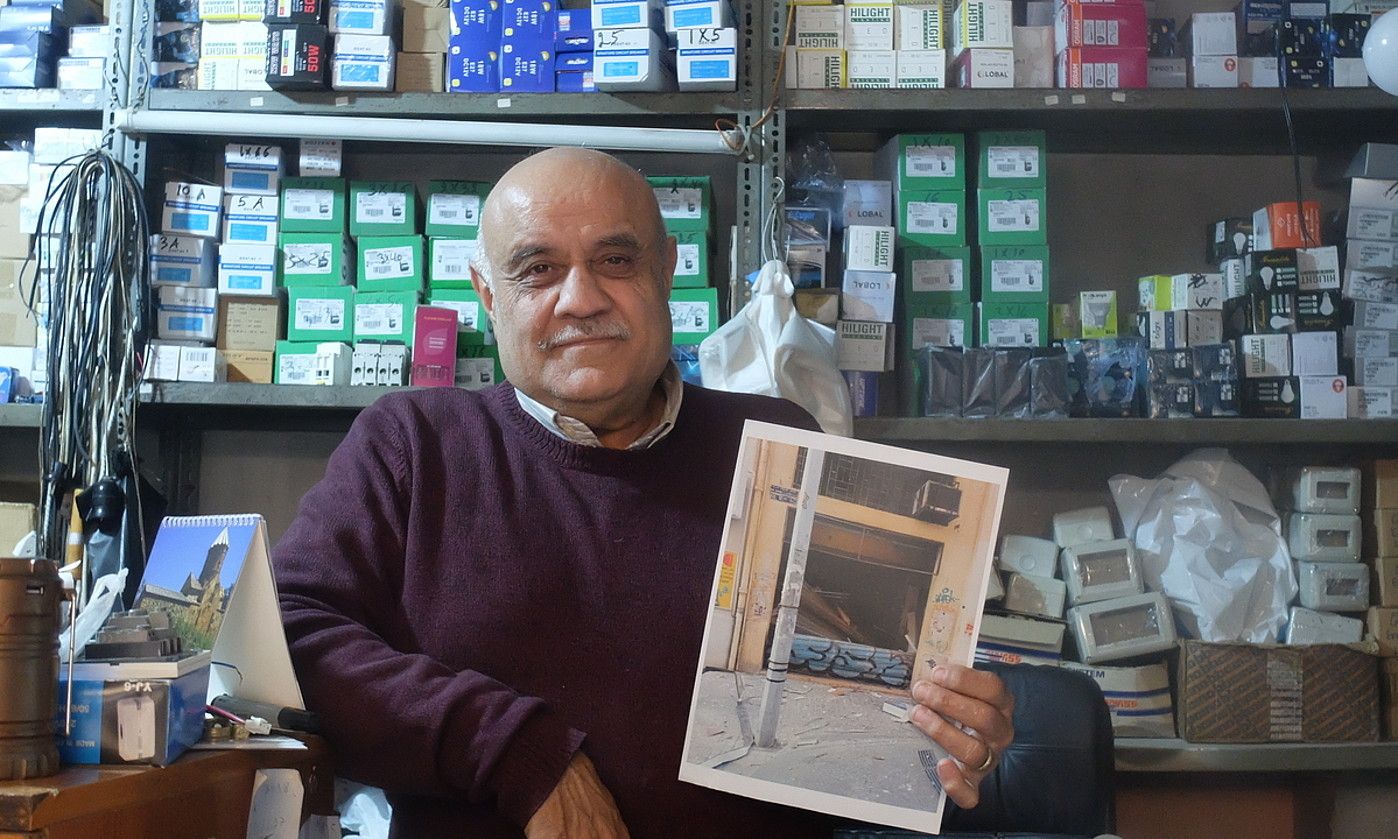 Vatxek, portuko leherketaren osteko dendaren argazki batekin eskuetan. J. C. V. Vatxek, portuko leherketaren osteko dendaren argazki batekin eskuetan. J. C. V.