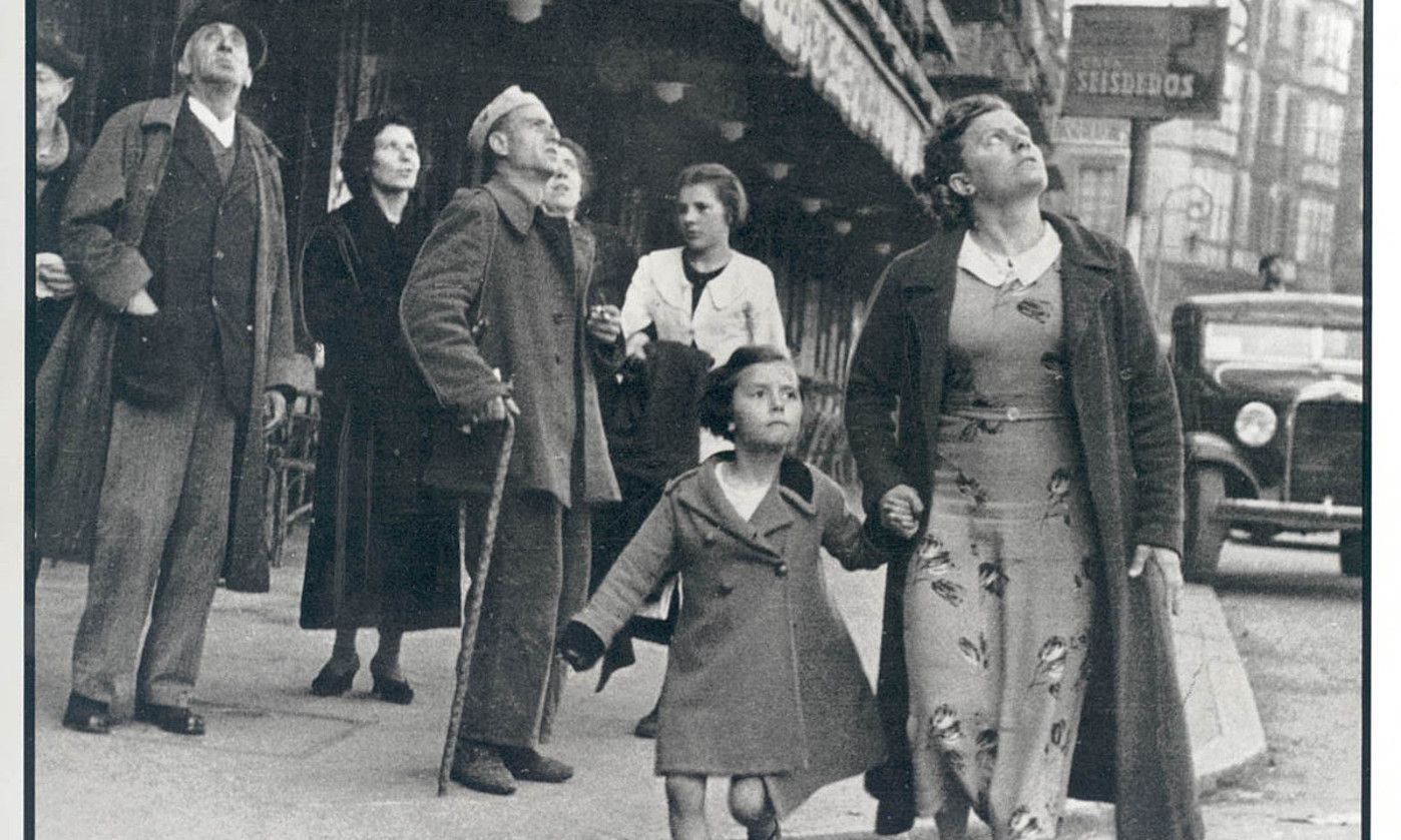 Jendea kezkaz zerura begira Bilboko kale batean, aire eraso baten esperoan. Robert Capa argazkilariaren irudia. BERRIA.