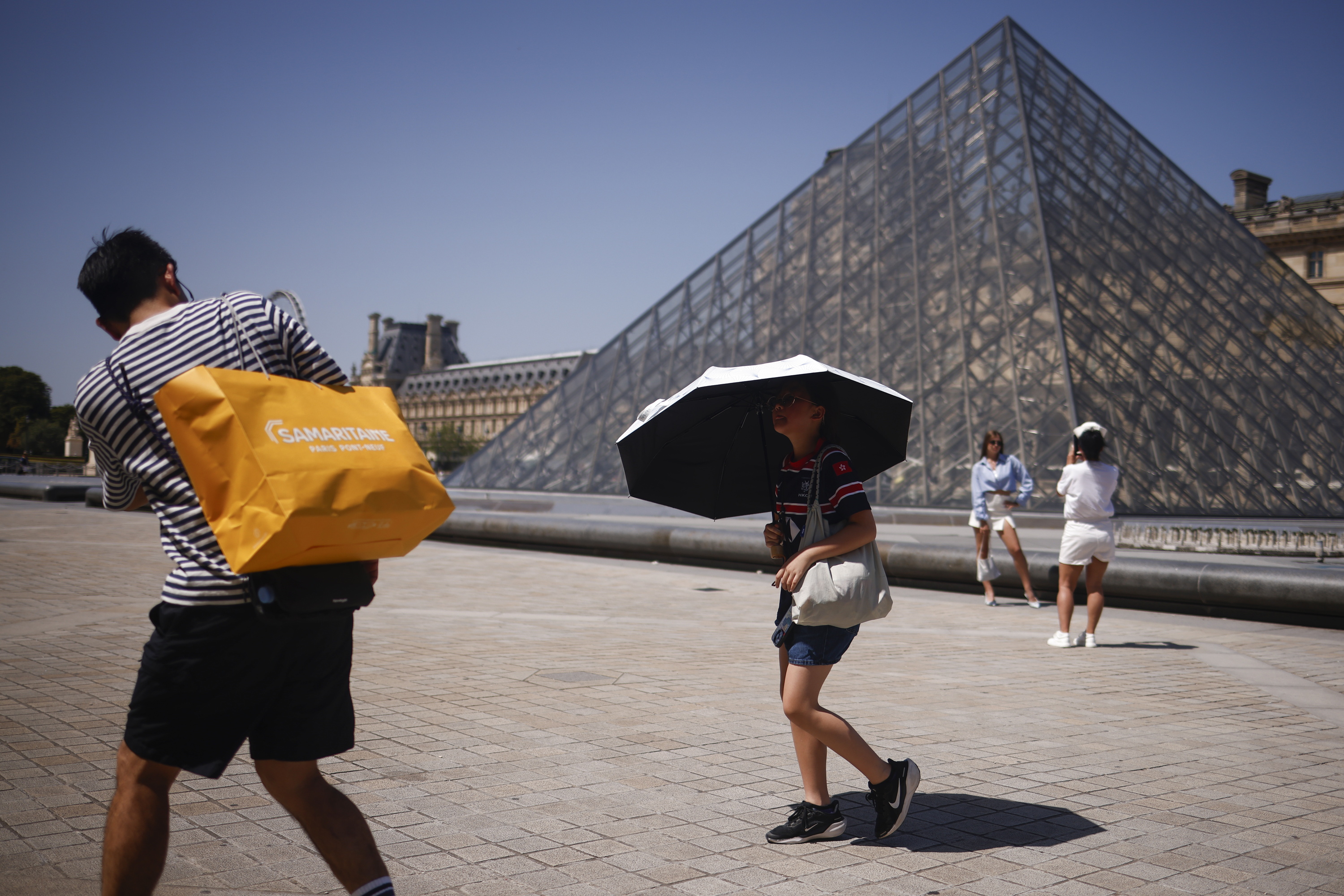Nerabe bat euritako batekin beroa uxatzeko, atzo, Parisko Louvre museoan. YOAN VALAT/EFE
