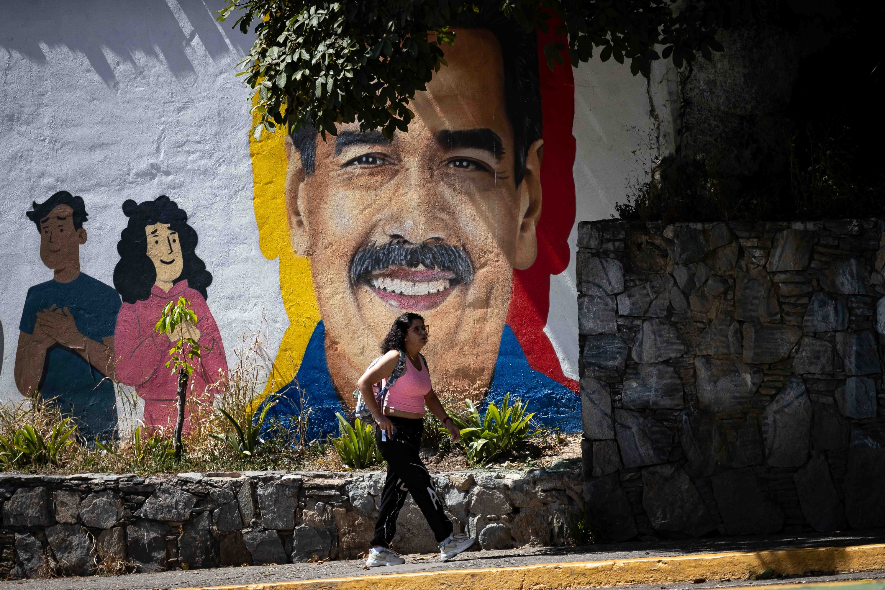 Pertsona bat Caracaseko kaleetan oinez, Nicolas Maduro Venezuelako presidentea marraztuta dagoen mural baten aurrean. RONALD PENA / EFE
