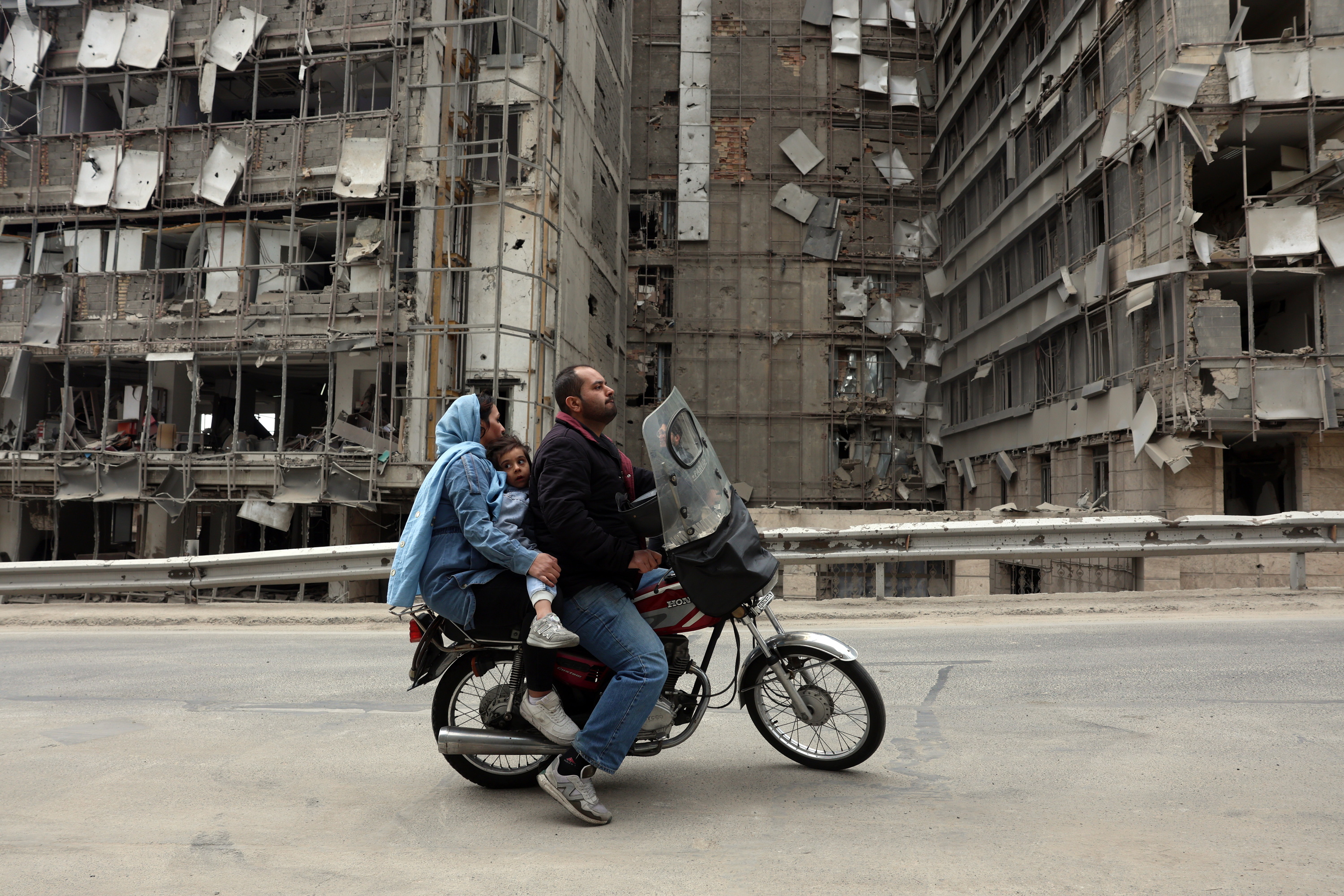 Hiru irandar atzo Teheranen, AEBen eta Israelen erasoek txikitutako eraikin baten paretik igarotzen. ABEDIN TAHERKENAREH / EFE