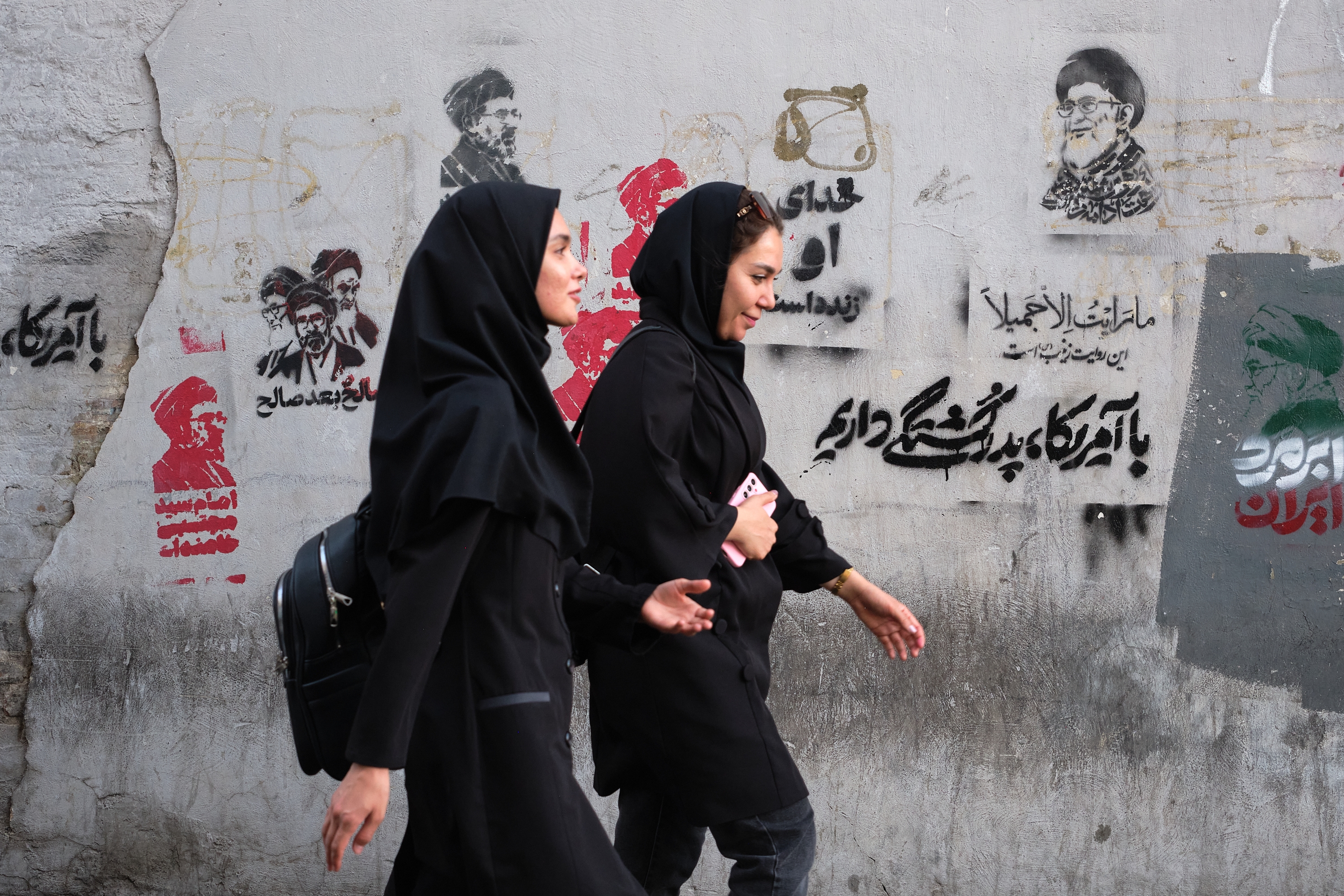 Bi emakume Ali Khamenei lider gorena izandakoaren eta haren oinordeko Mojtaba Khameneiren irudien ondotik igarotzen, Teheranen, atzo. JAIME LEON / EFE 
