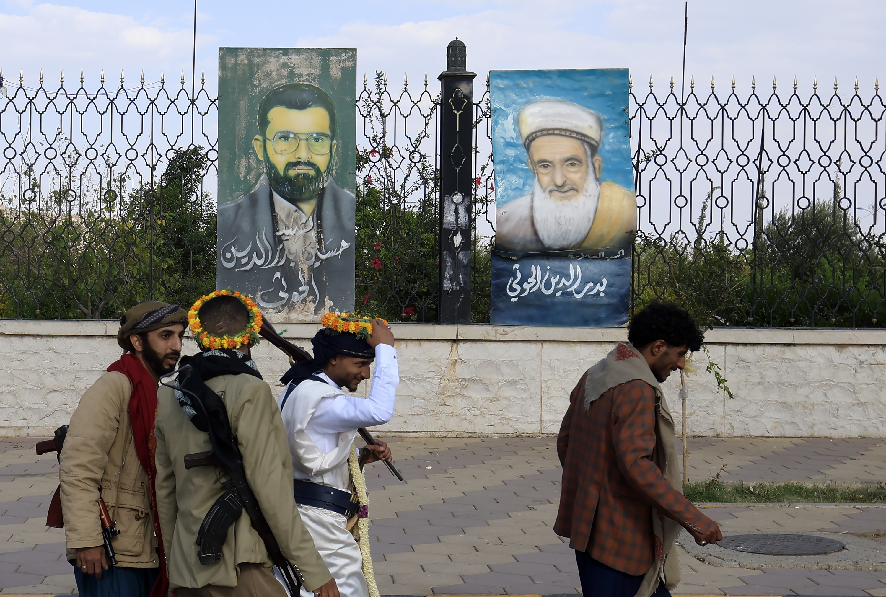   Armatutako pertsona talde bat garai bateko buruzagi huthiak irudikatzen dituzten koadro batzuen ondotik igarotzen, Sanan, Yemenen, atzo. YAHYA ARHAB / EFE 
